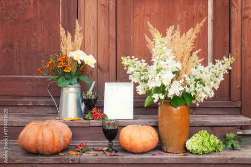 Frame, glasses of red wine, bouquet of white roses, helenium and dry grass, bouquet of hydrangea and dry grass, pumpkins and  hydrangea on steps of rustic wooden ladder.