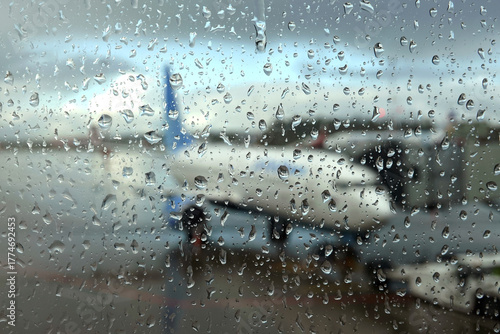 Blurred view to air field with aircraft through the glass with rain drops in the overcast weather in the evening