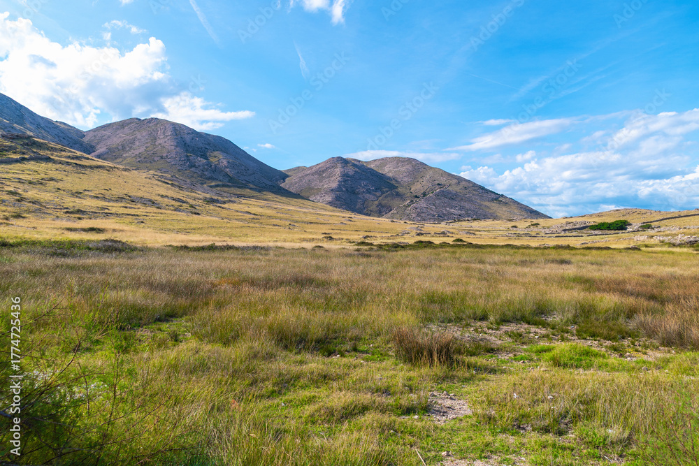Fototapeta premium Serene mountain landscape with blue sky and rolling hills. Vela Luka beach, Krk island, Croatia