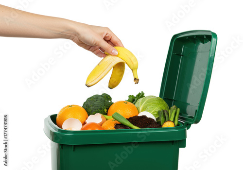A slender female hand gracefully drops a vibrant yellow banana peel into a forest-green compost bin overflowing with fresh organic waste against a stark white studio background, concept of ecological
