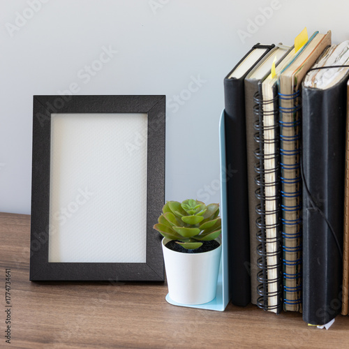 Blank Picture Frame with Notebooks and Succulent Plant on Wooden Shelf