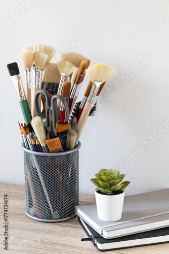 Art Brushes and Tools in Metal Holder on Wooden Desk with Succulent Plant