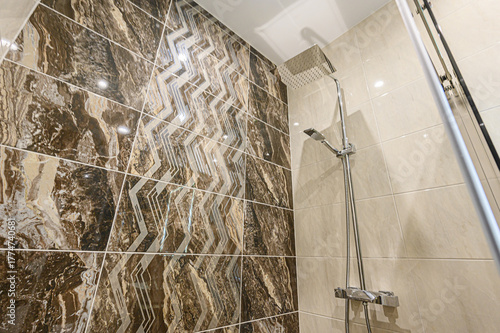 Modern shower with brown patterned tile on one wall and a shower with a large, square showerhead