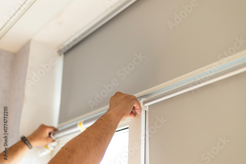 Male hands installing window blinds on modern window indoors.