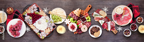 Christmas holiday charcuterie table scene on a dark wood banner background. Top down view. Variety of cheese, fruit and meat appetizers. © Jenifoto