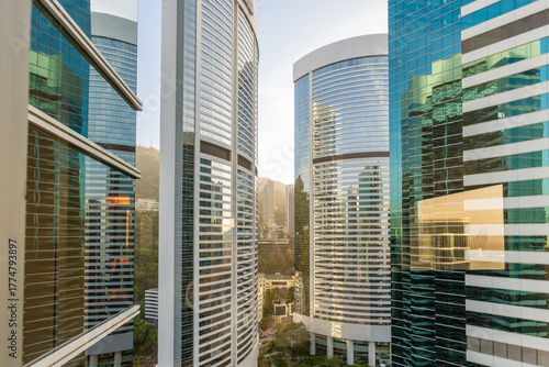 Modern skyscrapers reflecting urban landscape, Hong Kong. High-rise buildings with glass facades, financial district, vibrant cityscape, sunny day.