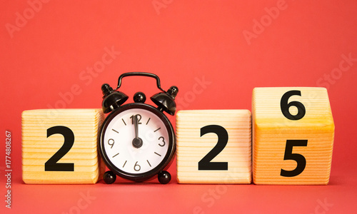 2026 New Year symbol. Businessman turns wooden cube and changes Year 2025 to 2026. Beautiful red background with Alarm clock. Copy space. Business and 2026 happy new year concept