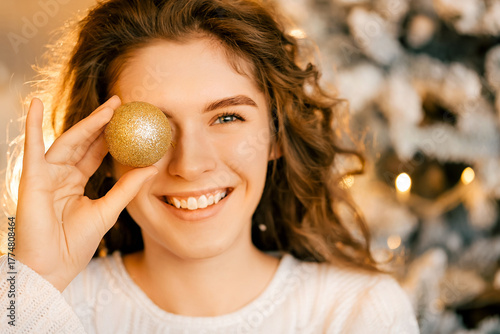beautiful curly girl in a white sweater with dark hair smiling. woman holding a Christmas toy, happy New Year portrait