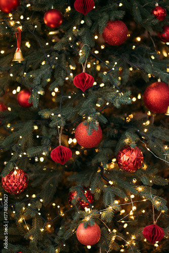 A close-up of a festive Christmas tree decorated with red ornaments, glowing fairy lights, and natural green pine needles.