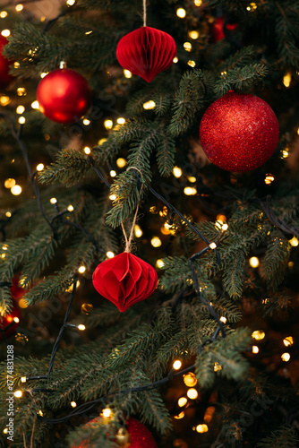 A close-up of a festive Christmas tree decorated with red ornaments, glowing fairy lights, and natural green pine needles.