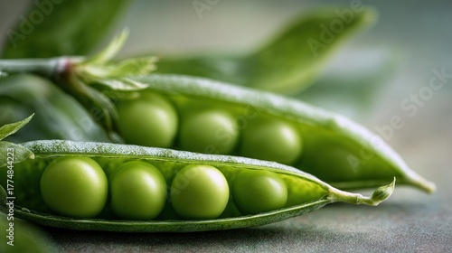   A pair of peas resting atop a green leaf with water droplets adorning them