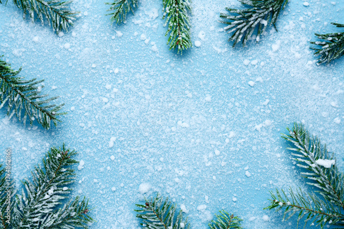 Frosty Christmas and New Year composition. Top view of green fir tree branches covered with snow on a blue background, forming a winter frame with copy space in the center.