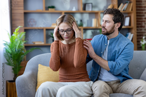 Photography Woman clutching temples in severe headache while partner sits close on sofa offe