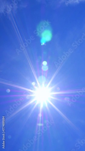 Bright sunlight streaming through a clear blue sky, creating a beautiful starburst effect and colorful lens flare. Warm sunbeams radiate across the serene atmosphere on a perfect summer day