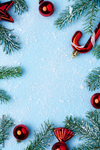 Christmas composition with red holiday ornaments and green fir branches covered with snow on a light blue background.