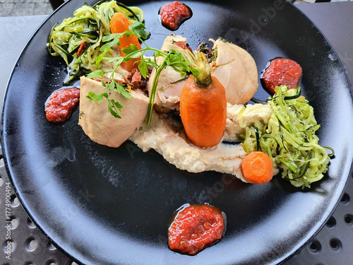 Gourmet plated dinner: Modern poultry dish with vegetable garnishes and red sauce dots on a black plate.