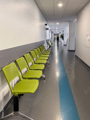 Modern hospital corridor featuring clean, spacious design with green chairs arranged for waiting patients, showcasing a welcoming and restful atmosphere in a healthcare environment