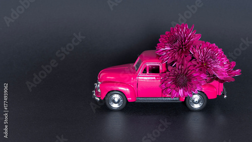 Cute old pink car carry violet flowers on black paper background