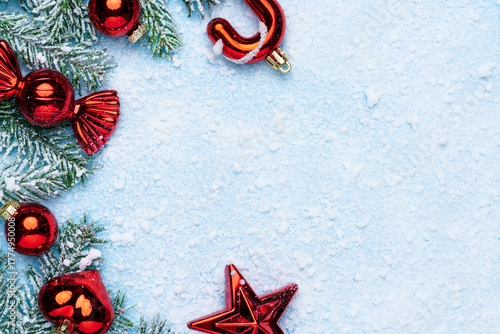 Festive Christmas composition with red ornaments, candy cane, and frosted fir branches on light blue snowy background.