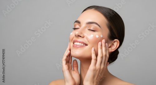 Young woman applying skincare cream with eyes closed, enjoying beauty routine on neutral background