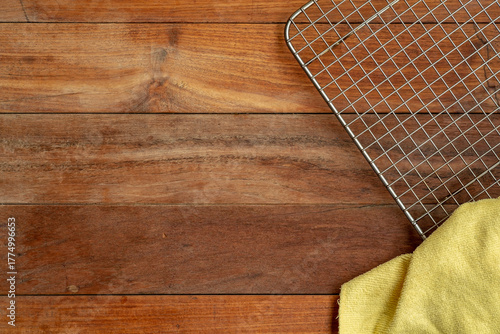 An overhead view of a dark, rustic wooden surface with a metal wire cooling rack and a yellow cloth placed in the right-hand corner.
