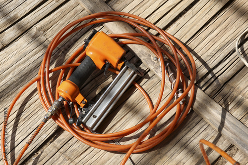 Photos Pneumatic nail gun with an orange extension cord resting on weathered wood deck