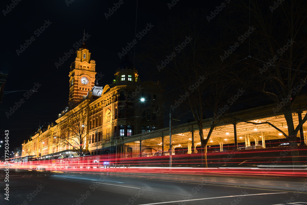 Fototapeta premium Melbourne, Australia, Night view of the historic Flinders Street Station with its iconic clock tower, featuring light trails from passing traffic on Flinders Street.