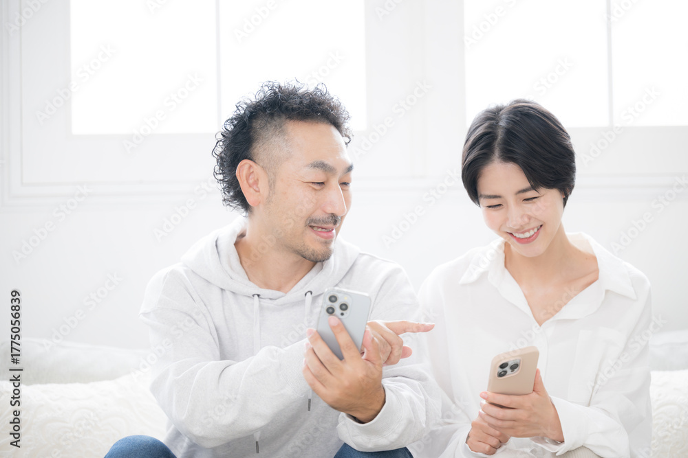 Obraz premium リビングでスマホを見るミドルの笑顔の夫婦やカップル