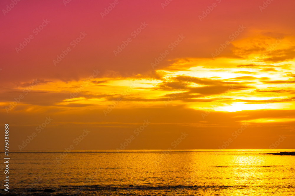 Obraz premium Nature sky breathtaking golden sunset over a calm ocean, with the entire sky and water bathed in brilliant shades of yellow and orange. Streaky clouds enhance the dramatic display of light 