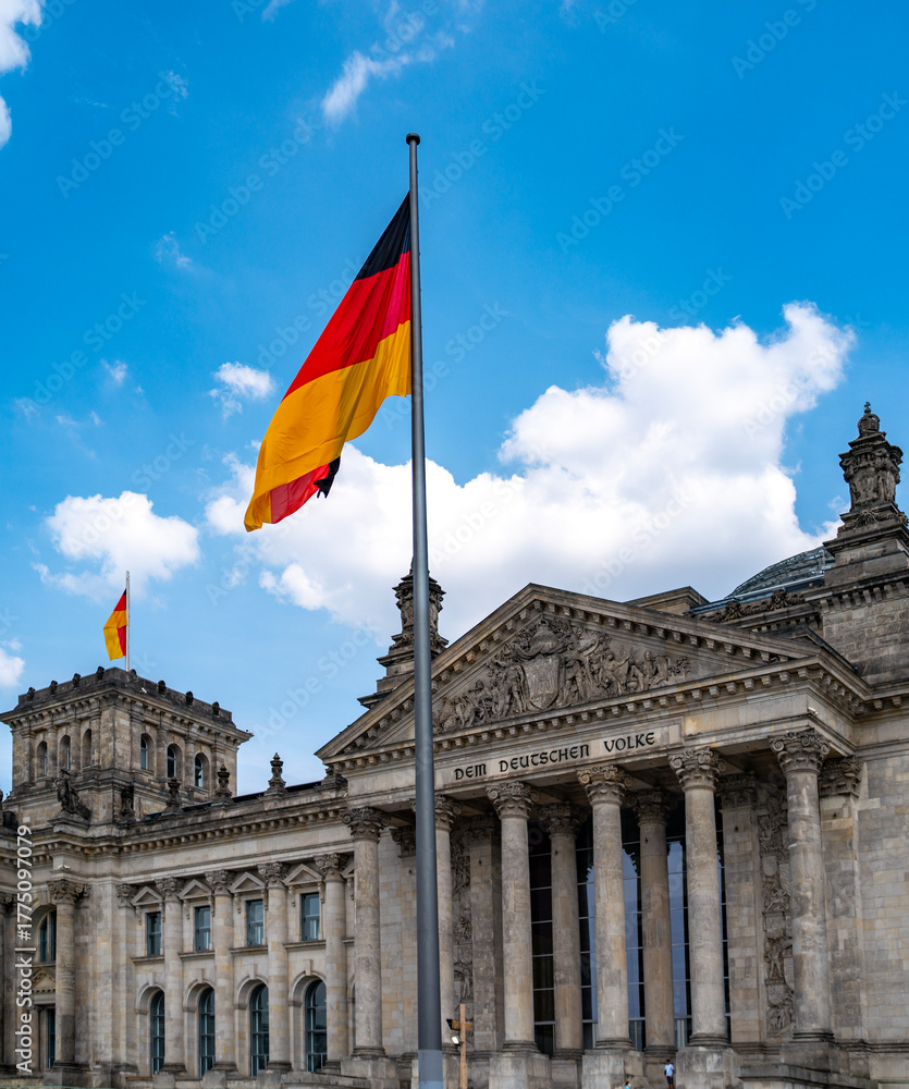 Obraz premium German flag waving above Reichstag. Symbol of unity and democracy. Blue sky and national pride. Landmark of Berlin. Reichstag Political symbol of Germany. German flag over Reichstag.