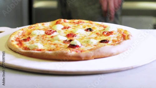 Pizzas transferring hot, Fresh baked pizza being moved, Closeup of hot pizza transfer to serving board, Busy kitchen scene with steaming pizza being placed onto wooden