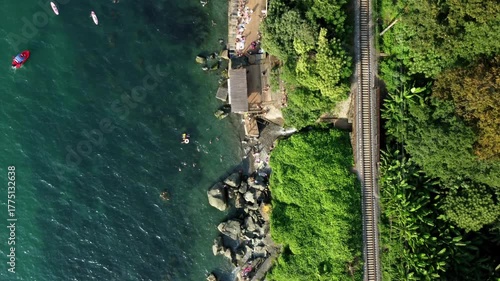 Seaside train scenery, Coastal railway over lively beach, Elevated train above bustling waterfront area, Aerial railway traversing vibrant seaside with active harbor