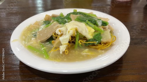 a plate of Capcay, an Indonesian-Chinese stir-fried vegetable dish, served with thick savory gravy, egg, and crispy noodles on a white plate. 