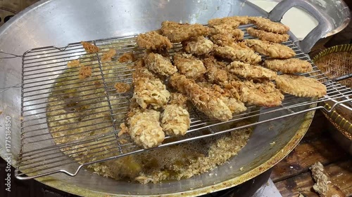 a batch of golden brown pisang goreng (Indonesian fried bananas) draining on a rack over a large wok filled with hot oil.