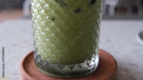 Smooth panning video capturing a refreshing iced matcha latte in a patterned glass, placed on a wooden coaster over a terrazzo tabletop.
