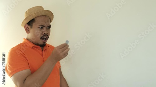 surprised man in an orange shirt and hat holding a single coin, expressing shock and disbelief over having little money.