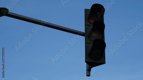 a traffic signal suspended on a pole showing a yellow light, captured during daylight with a clear blue sky in the background.  