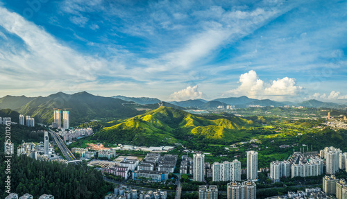 Fotografie Aerial panorama of Shenzhen city edge where urban developments and highways meet lush green mountains under a dramatic cloudy sky