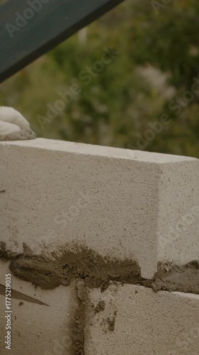 Vertical Screen: A worker skillfully builds a sturdy wall using concrete bricks to contribute to a new house construction project. Focus on craftsmanship and attention to detail.