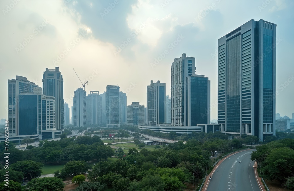 Fototapeta premium Urban skyline view of Gurugram in India shows tall contemporary buildings. Modern corporate architecture rises beyond green trees. Road stretches towards city center at daytime. Business district