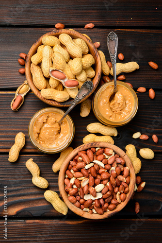 Peanut butter in glass jar and spoon. Roasted peanuts in the shell. American dessert concept. Homemade nut butter. Vertical photo.