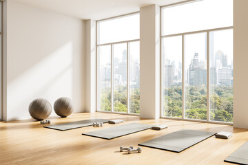 Fototapete Yogaschule Bright yoga studio interior design with large windows, scenic city view, exercise mats, dumbbells, and fitness balls on wooden floor. 3D Rendering  © ImageFlow