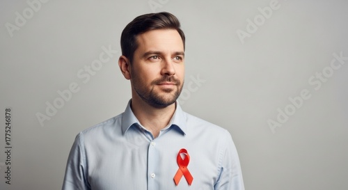 A hopeful-looking man with a beard, wearing a red awareness ribbon on his shirt for HIV/AIDS support.