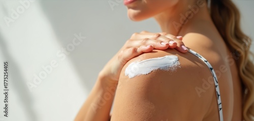 Woman applies white cream to shoulder, protecting skin from sun. Close up of hand smoothing lotion on sun tanned skin. Summer care for healthy body outdoors. Sunscreen application for skin protection.