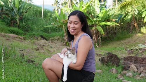 A happy young woman is sitting while holding a cat on her lap. 