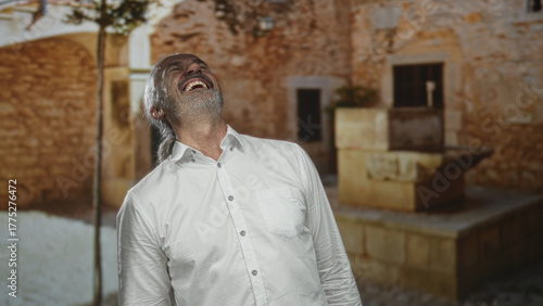 Photography Man with hoary long hair and beard laughing with head tilted back, face visible on old town street; joy contentment wisdom