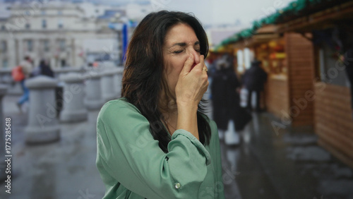 Fotografija Middle aged hispanic woman pinches nose near souvenir stall at crowded city street market; disgust discomfort