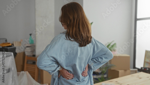 Slika na platnu Woman standing in a new home surrounded by moving boxes and furniture, wearing casual attire, thoughtful about arrangements in a bright, modern living room with plants and decor
