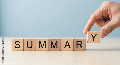 Hand placing the final letter y on wooden blocks spelling out the word summary