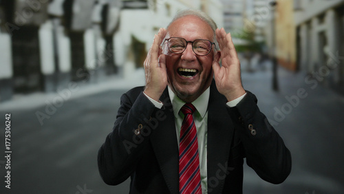 Fotografija Senior man in suit laughing with hands on face in outdoor street setting, portraying business success and happiness